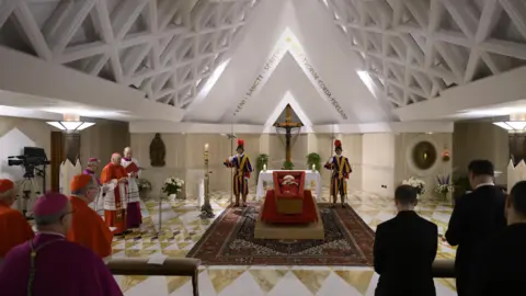 EPA-IFE/Rex/Shutterstock يكمن جسم البابا فرانسيس في نعش مفتوح في مصلى سانتا مارتا ، مدينة الفاتيكان ، محاطًا بحراس سويسريين وكرادلة في الصلاة.