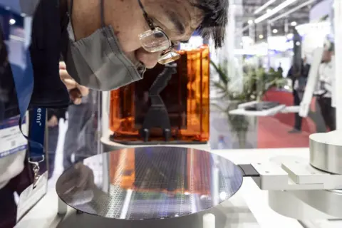 Getty Images رجل يرتدي نظارات وقناع الوجه ينحني للنظر في رقاقة أشباه الموصلات الدائرية