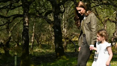 رويترز كاثرين تحمل يد فتاة صغيرة في ثوب أبيض وهم يمشون عبر الغابة