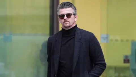 PA Media Joey Barton ، في الظلال ومعطف أزرق داكن طويل ، يخرج من مبنى المحكمة. 