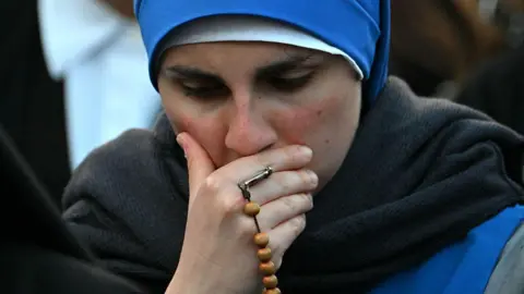Getty Images تمسك امرأة وجهها ، مع حبات الصلاة ملفوفة حول أصابعها بينما تنعى للبابا فرانسيس في ساحة القديس بطرس بعد خبر وفاته في 21 أبريل 2025.