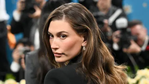 Getty Images Hailey Bieber في حفل Met 2025. إنها ترتدي فستانًا أسود مع أقراط. 