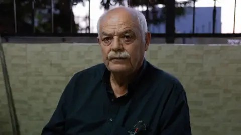 بي بي سي كاسيم أبو الحجة يجلس في وقفة لأفراد عائلته. إنه رجل في الستينيات من عمره مع شارب رمادي