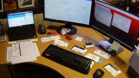 National Trading Standards A photo provided by National Trading Standards showing the Ticket Queen's office, with an L-shape desk with two computer monitors and a laptop, piles of tickets neatly arranged on the desk, along with office stationery and a calculator.